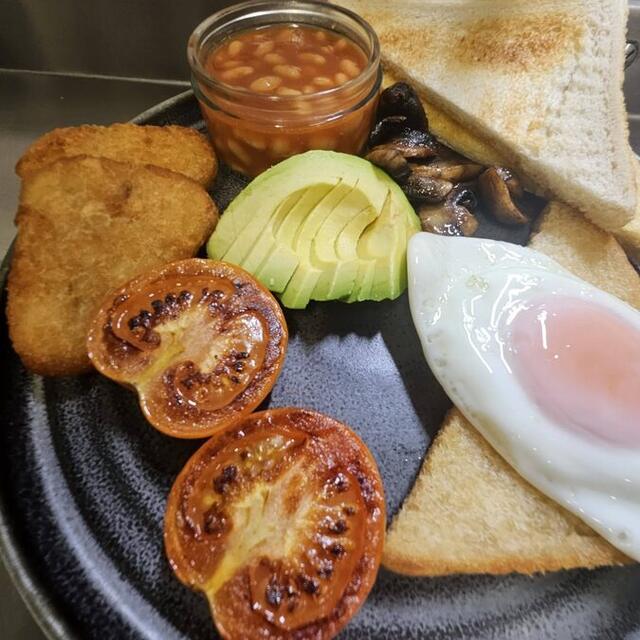 Cooked breakfast plate with fried egg, hash browns, grilled tomato, avocado, mushrooms and beans